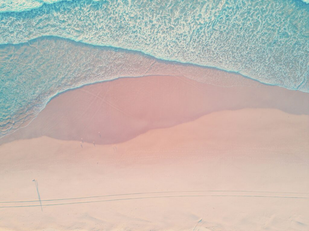 Aerial view of a serene beach with soft waves and pastel sand, evoking the calm and beauty of coastal destinations near Galveston